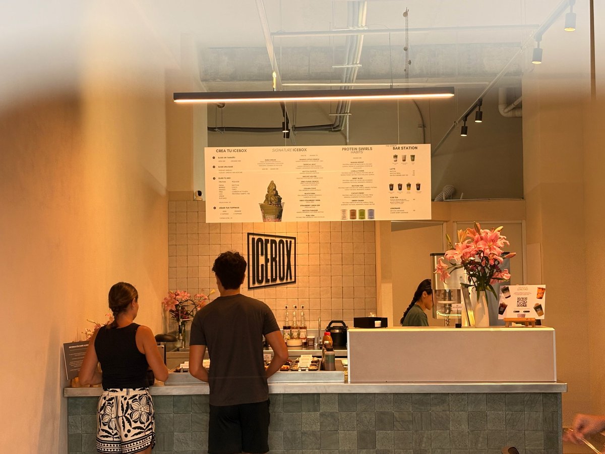 Interior of a modern coffee shop with customers at the counter and a menu board illuminated above